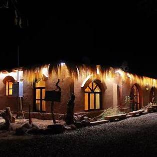 Espacio común al aire libre de un hostal económico en San Pedro de Atacama, con mesas, vegetación y arquitectura típica del desierto, ideal para viajeros baratos.